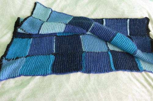 a blanket made of knitted patches in different shades of blue; same blanket as on the header picture